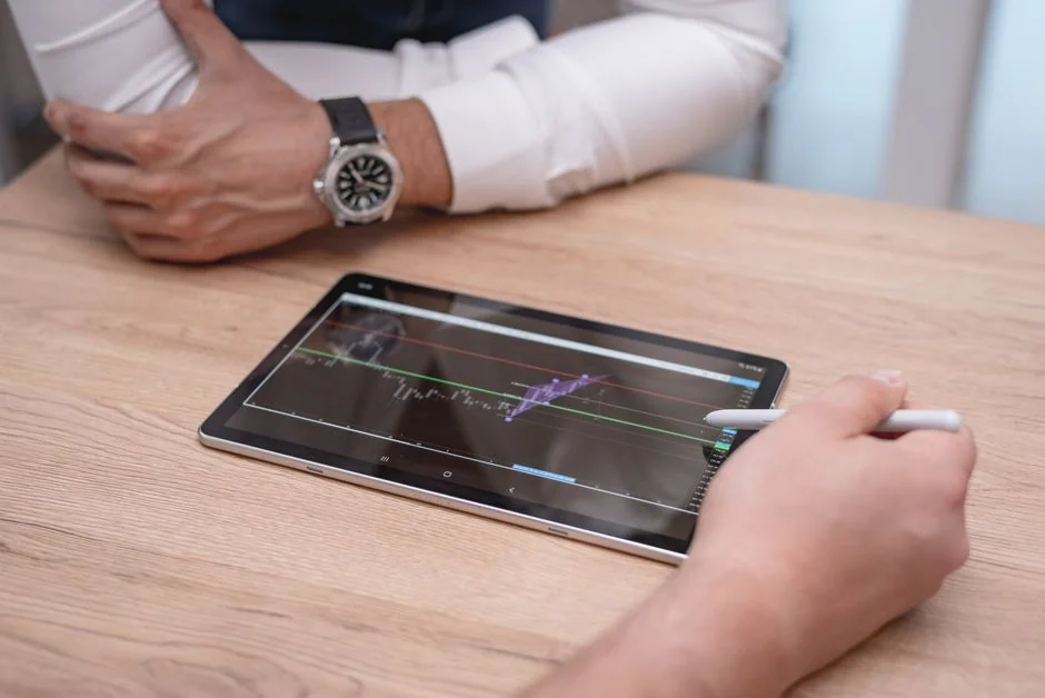 Two businessmen analyze stock market data using a smartphone and laptop in a modern office setting.